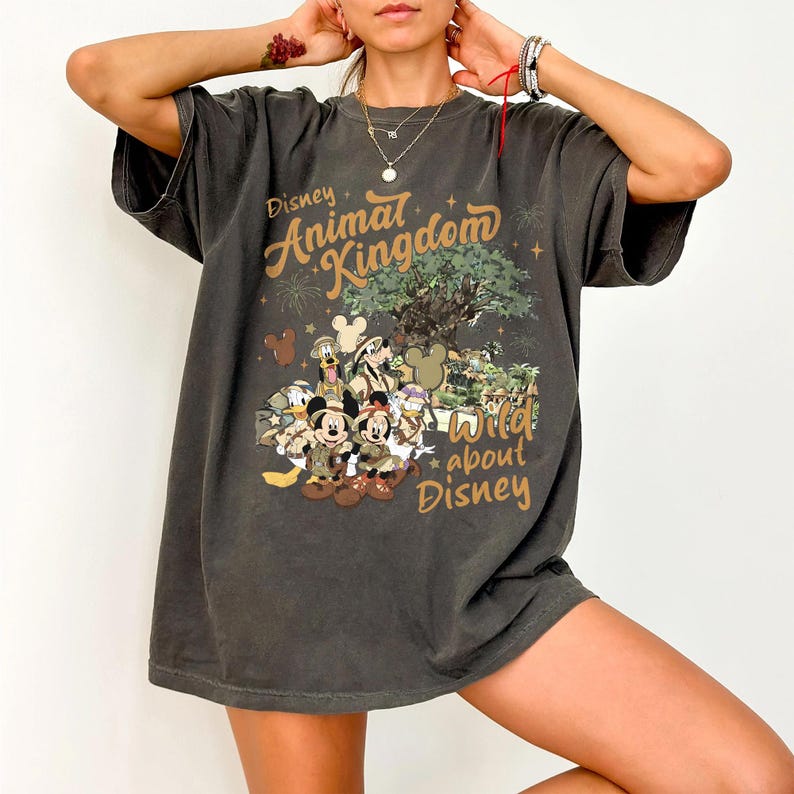 Pu&ograve; includere: T-shirt grigio scuro con la scritta "Disney Animal Kingdom" e "Wild about Disney". La grafica presenta personaggi Disney, tra cui Topolino e Minnie, in tenute da safari. La maglietta ha una vestibilit&agrave; ampia e uno stile casual.
