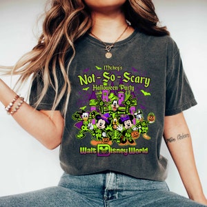 May include: Dark gray t-shirt featuring a graphic for Mickey's Not-So-Scary Halloween Party at Walt Disney World. The design includes Mickey Mouse, Minnie Mouse, Donald Duck, and Goofy in skeleton costumes, with a purple castle and green accents.