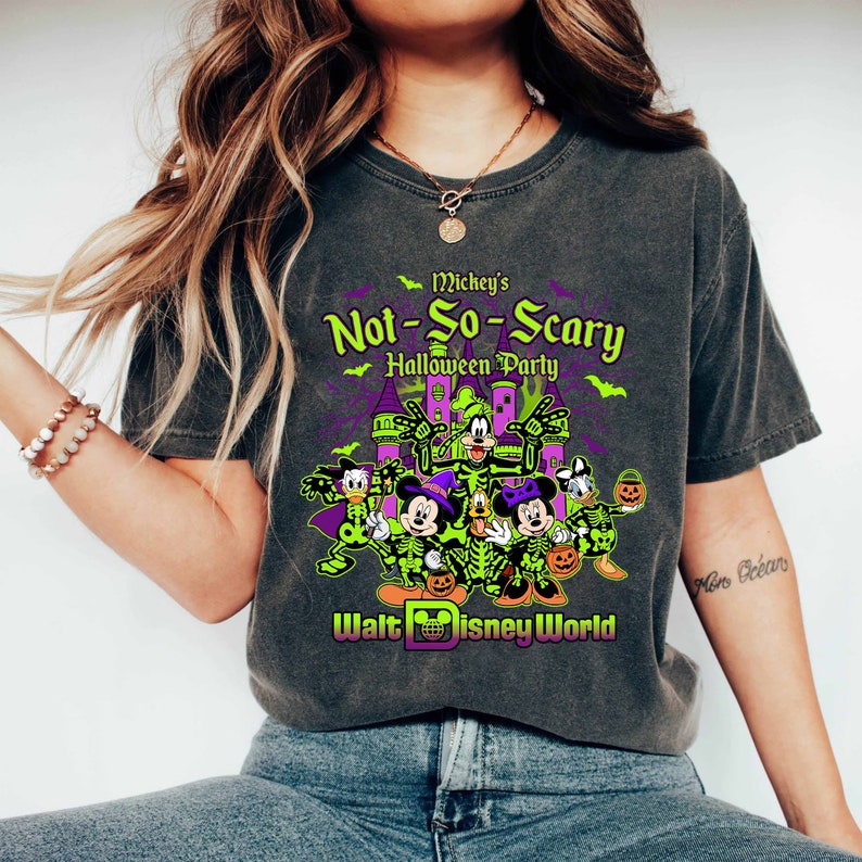 May include: Dark gray t-shirt featuring a graphic for Mickey's Not-So-Scary Halloween Party at Walt Disney World. The design includes Mickey Mouse, Minnie Mouse, Donald Duck, and Goofy in skeleton costumes, with a purple castle and green accents.