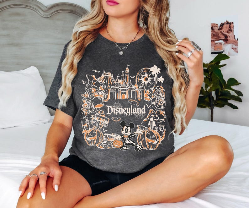 May include: Dark gray t-shirt featuring a Disneyland design with orange and white graphics. The design includes a castle, Ferris wheel, pumpkins, and Mickey Mouse. The word "Disneyland" is prominently displayed.