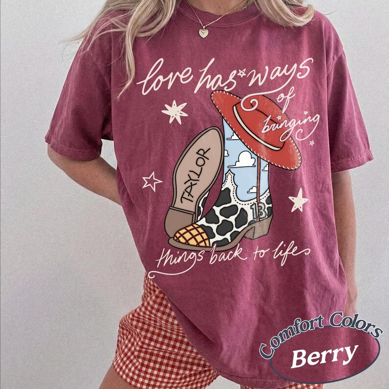May include: A berry-colored short-sleeve t-shirt featuring a graphic of a cowboy boot with a cow print pattern, a red hat, and the text "love has ways of bringing TAYLOR 13 things back to life" with small star accents printed on the front.