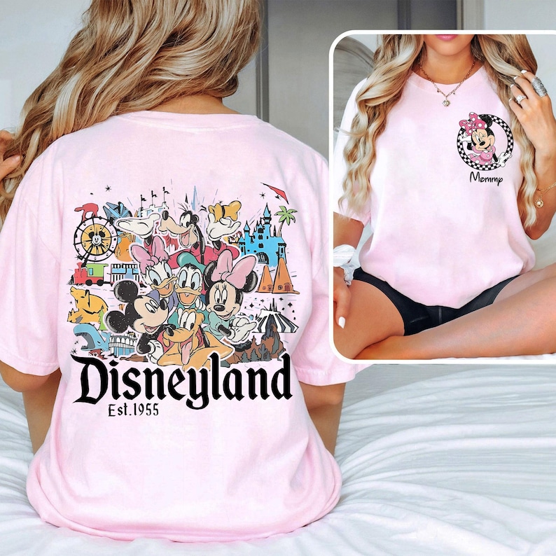May include: Pale pink t-shirt with a Disneyland graphic featuring Mickey Mouse, Minnie Mouse, Donald Duck, and other Disney characters. The shirt also has the text "Disneyland Est. 1955". A smaller image of Minnie Mouse is on the front.