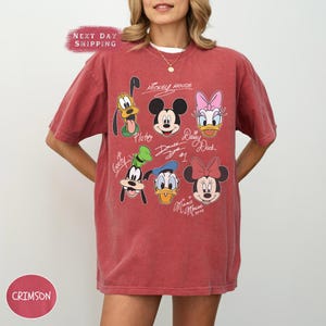 May include: Red t-shirt with a vintage-style graphic of Mickey Mouse, Minnie Mouse, Donald Duck, Daisy Duck, Goofy, and Pluto. The graphic includes the characters' names and signatures.