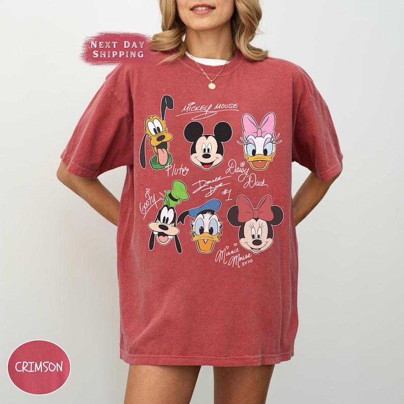 May include: Red t-shirt with a vintage-style graphic of Mickey Mouse, Minnie Mouse, Donald Duck, Daisy Duck, Goofy, and Pluto. The graphic includes the characters' names and signatures.