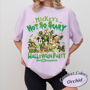 K&ouml;nnte beinhalten: Orchideenfarbenes T-Shirt mit einem Halloween-Motiv mit Disney-Figuren. Das Design enth&auml;lt den gr&uuml;nen Text "Mickey's Not So Scary Halloween Party" sowie Cartoon-Figuren in Skelett-Kost&uuml;men. Das T-Shirt ist von Walt Disney World.
