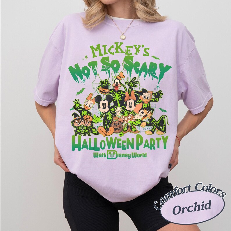 K&ouml;nnte beinhalten: Orchideenfarbenes T-Shirt mit einem Halloween-Motiv mit Disney-Figuren. Das Design enth&auml;lt den gr&uuml;nen Text "Mickey's Not So Scary Halloween Party" sowie Cartoon-Figuren in Skelett-Kost&uuml;men. Das T-Shirt ist von Walt Disney World.