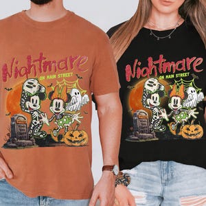 May include: Two t-shirts, one orange and one black, featuring a Halloween-themed graphic. The design includes Mickey and Minnie Mouse dressed as skeletons, a pumpkin, and the text "Nightmare on Main Street."