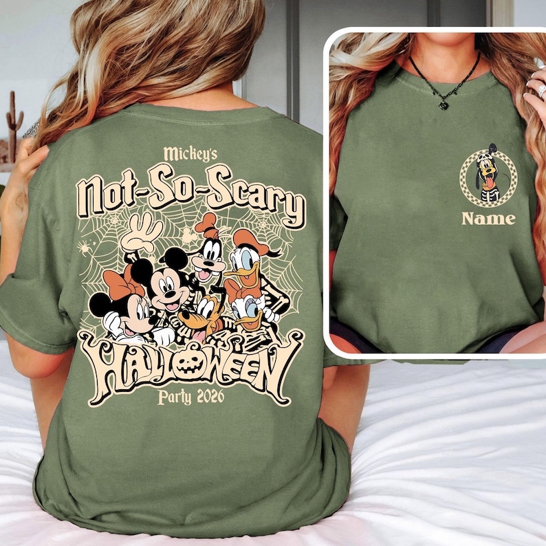 May include: Olive green t-shirt featuring a Halloween design with Mickey Mouse, Minnie Mouse, Goofy, Donald Duck, and Pluto. The shirt has the text "Mickey's Not-So-Scary Halloween Party 2026". A smaller image of Goofy is on the front.