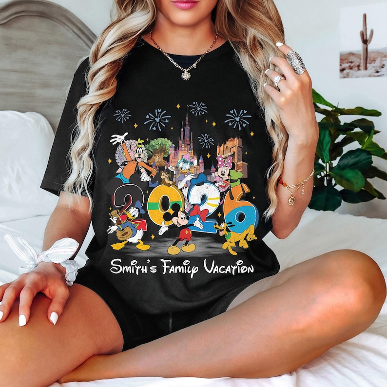 Może przedstawiać: Czarny t-shirt z kolorową grafiką postaci Disneya i numerem "2026". Projekt zawiera Myszka Miki, Kaczora Donalda i inne postacie, z tekstem "Smith's Family Vacation" poniżej.