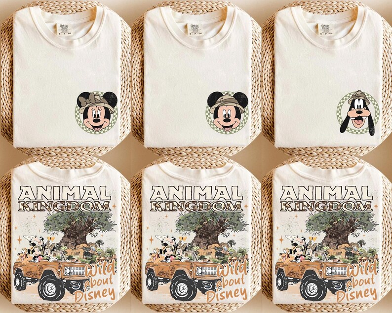 May include: Cream-colored t-shirts featuring Mickey Mouse and Goofy in safari hats, and the text "Animal Kingdom Wild about Disney." The shirts are folded on woven mats, showcasing a theme of adventure and Disney characters.