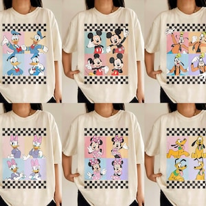 May include: Cream-colored t-shirts featuring colorful cartoon character designs. Each shirt showcases a different set of characters, including Donald Duck, Mickey Mouse, Goofy, Daisy Duck, Minnie Mouse, and Pluto, set against a checkered background.