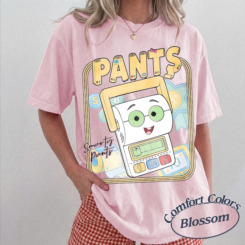 May include: A light pink short-sleeve t-shirt featuring a graphic of a cartoon calculator with a toilet paper roll face, green glasses, and a pink bow. The text reads "PANTS" and "Smarty Pants" with numbers and blue ribbon icons in the background.