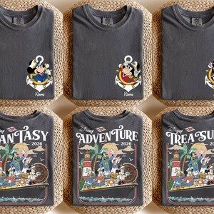 Puede incluir: Seis camisetas de color gris oscuro con dise&ntilde;os de personajes de Disney. Tres camisetas presentan a Mickey Mouse en un dise&ntilde;o de ancla, con la palabra "Name" debajo. Las otras tres camisetas tienen un dise&ntilde;o de crucero con las palabras "Fantasy 2026", "Adventure 2026" y "Treasure 2026".