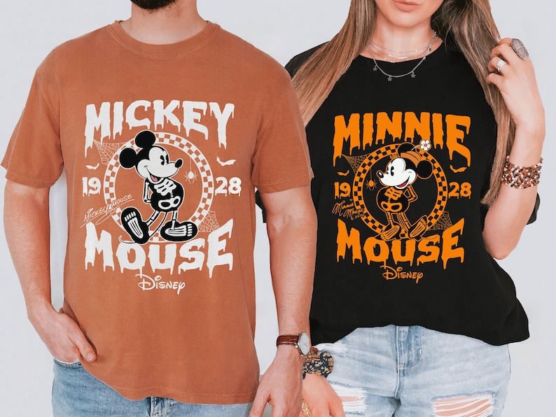 May include: Two t-shirts, one brown and one black, featuring Halloween-themed Mickey and Minnie Mouse designs. The designs include a skeleton Mickey and Minnie, the text "Mickey Mouse" and "Minnie Mouse", and the Disney logo.