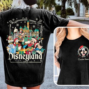 May include: Black t-shirt featuring a Disneyland Christmas design. The back of the shirt displays a colorful graphic with Mickey Mouse, Donald Duck, and other characters in front of a castle. The front has a Mickey Mouse graphic with the text "Custom Name".