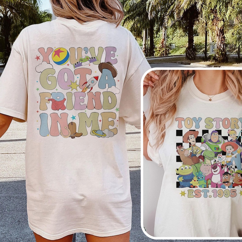 May include: White t-shirt with a colorful graphic on the back that says "You've Got a Friend in Me" with a cartoon rocket, cowboy hat, and stars. The front of the shirt has a black and white checkered pattern with cartoon characters from Toy Story and the text "Toy Story Est. 1995".