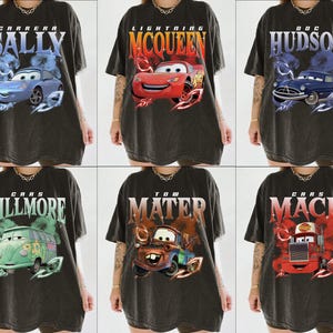 May include: Six black t-shirts with different Cars characters printed on them. The characters include Lightning McQueen, Mater, Mack, Doc Hudson, Sally, and Fillmore.