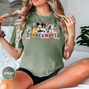 Pode incluir: Uma camiseta verde com lavagem vintage apresentando um gr&aacute;fico de Mickey Mouse e seus amigos com o texto "Disneyworld".