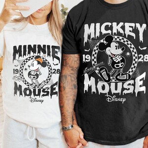 May include: White and black t-shirts featuring Mickey and Minnie Mouse in a Halloween skeleton design. The shirts have the text "Mickey Mouse" and "Minnie Mouse" with the Disney logo. The design includes the years 1928 and a spider web.