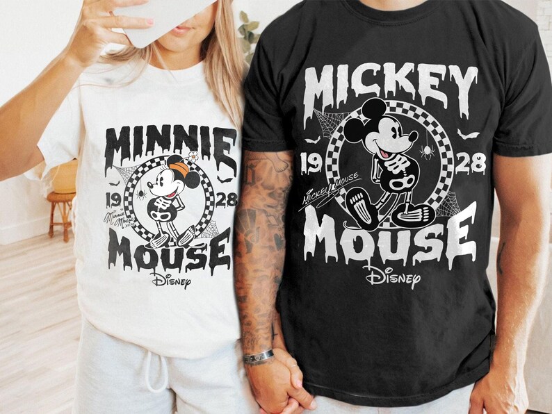 May include: White and black t-shirts featuring Mickey and Minnie Mouse in a Halloween skeleton design. The shirts have the text "Mickey Mouse" and "Minnie Mouse" with the Disney logo. The design includes the years 1928 and a spider web.