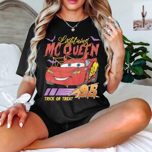 May include: Black t-shirt featuring Lightning McQueen from the movie Cars. The design includes the text "Lightning McQueen" in red and yellow, with the number "95" and the phrase "Trick or Treat".