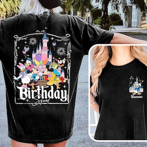 K&ouml;nnte beinhalten: Schwarzes T-Shirt mit einer farbenfrohen Grafik von Disney-Figuren, die einen Geburtstag vor einem Schloss feiern. Der Text "Birthday Squad" wird unter der Grafik angezeigt. Ein kleineres Bild von Donald Duck befindet sich auf der Vorderseite des T-Shirts.