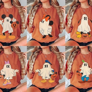 Peut inclure: Six t-shirts orange-brun repr&eacute;sentant des personnages de dessins anim&eacute;s d&eacute;guis&eacute;s en fant&ocirc;mes pour Halloween. Les personnages incluent Mickey Mouse, Minnie Mouse, Pluto et Donald Duck, chacun tenant une citrouille. Les chemises sont de style d&eacute;contract&eacute; et confortable.