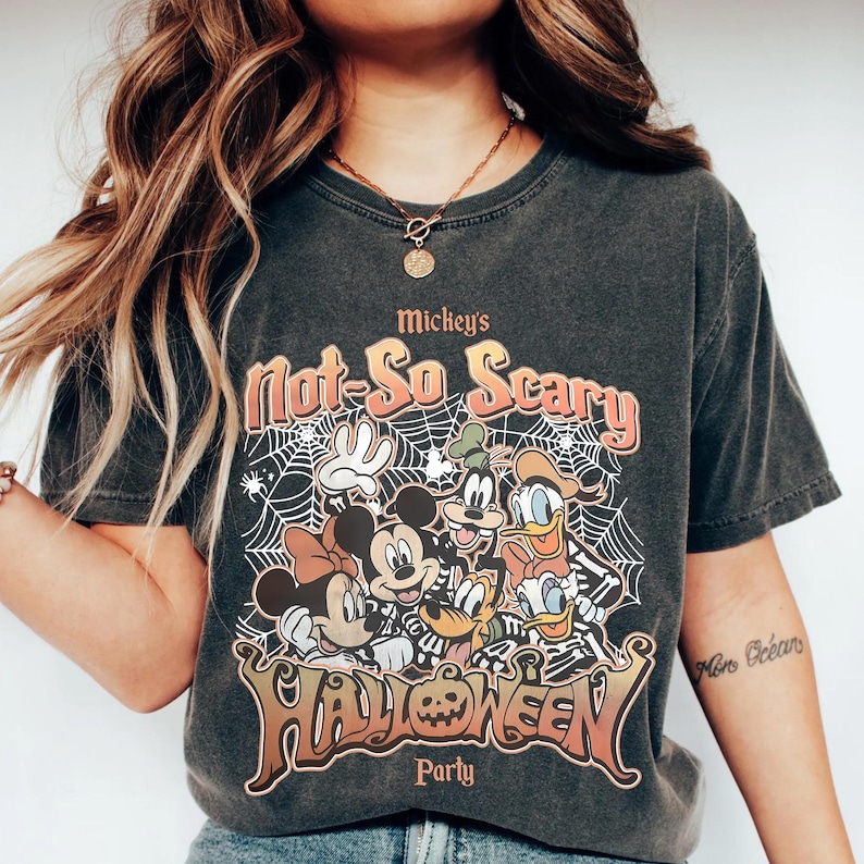 Puede incluir: Camiseta gris oscuro con un dise&ntilde;o de Halloween con Mickey Mouse y sus amigos. La camiseta muestra el texto "Mickey's Not-So Scary Halloween Party" en naranja y marr&oacute;n, sobre un fondo de telara&ntilde;a.