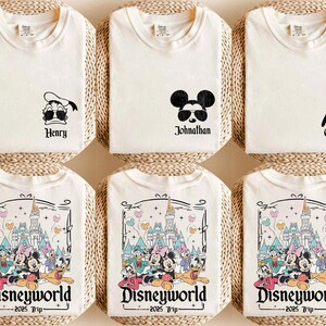 May include: Six white t-shirts with different designs. The designs include a cartoon duck, Mickey Mouse, Goofy, and a group of Disney characters in front of Cinderella's Castle. The text on the shirts reads "Henry", "Johnathan", "Custom", and "Disneyworld - 2025 Trip - "