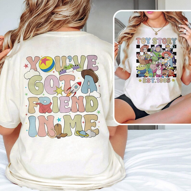 May include: White t-shirt with a colorful graphic that says "You've Got a Friend in Me" with a cartoon rocket, cowboy hat, and other images. The back of the shirt has a black and white checkered design with the text "Toy Story Est. 1995" and cartoon characters from the movie.