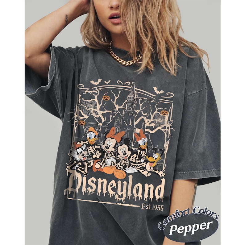 May include: Dark gray t-shirt featuring a Halloween-themed Disneyland graphic. The design includes Mickey Mouse, Minnie Mouse, Donald Duck, and Goofy as skeletons in front of a haunted house. The text "Disneyland" and "Est. 1955" are also visible.