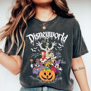 May include: Dark gray t-shirt featuring a Halloween-themed Disney World graphic. The design includes Disney characters dressed in costumes, a carved pumpkin, bats, and the text "Disneyworld".