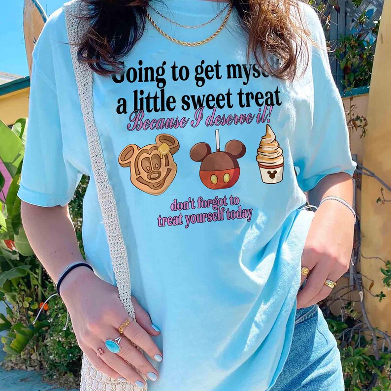 Puede incluir: Camiseta azul claro con el texto "Going to get myself a little sweet treat Because I deserve it!" e ilustraciones de un gofre, una manzana con caramelo y un helado de crema. La camiseta tambi&eacute;n tiene el texto "don't forget to treat yourself today."