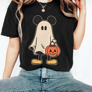 May include: Black t-shirt with a vintage-style illustration of a ghost wearing Mickey Mouse ears and holding a jack-o'-lantern.