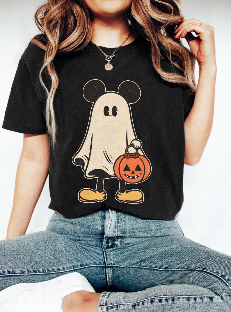 May include: Black t-shirt with a vintage-style illustration of a ghost wearing Mickey Mouse ears and holding a jack-o'-lantern.