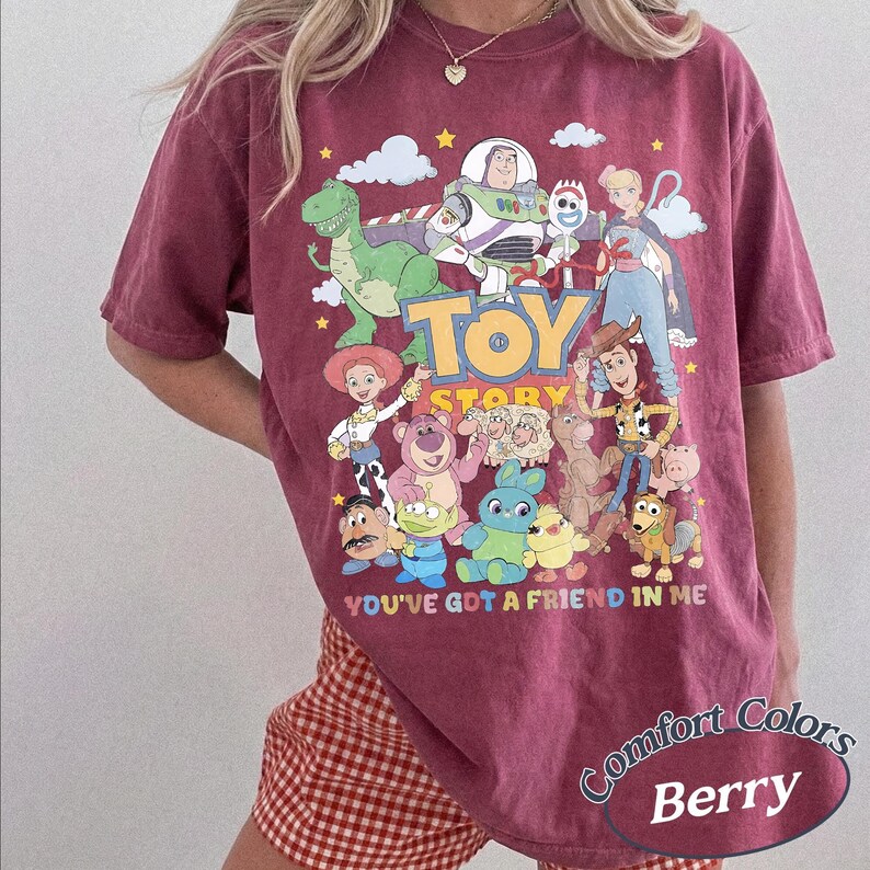 May include: A berry-colored short-sleeve t-shirt featuring a graphic print of various Toy Story characters including Woody, Buzz Lightyear, and Jessie. The text "TOY STORY" and "YOU'VE GOT A FRIEND IN ME" is printed in colorful letters on the front.