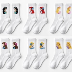May include: White crew socks with embroidered portraits of animated princesses. Each sock features a different princess, with details like hair colour and accessories. The socks are arranged in pairs, showcasing various princess designs.