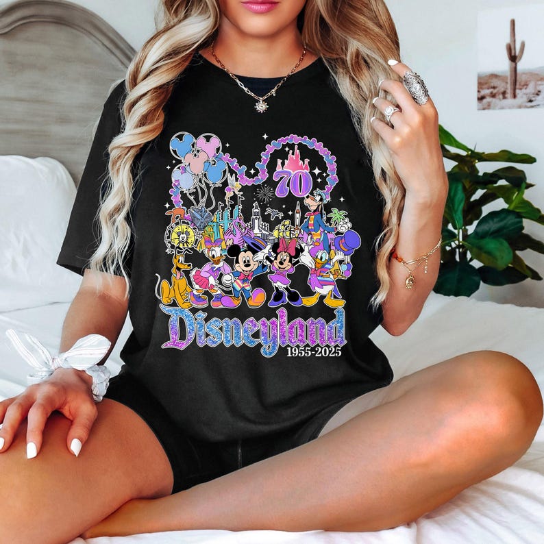 May include: Black t-shirt featuring a colorful Disneyland graphic. The design includes Mickey and Minnie Mouse, Donald Duck, and other Disney characters, along with the text "Disneyland 1955-2025" and the number "70".