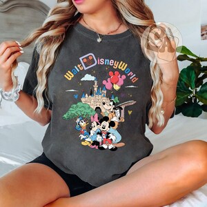 May include: A gray t-shirt with a vintage-style graphic of Mickey Mouse, Minnie Mouse, Donald Duck, and Goofy in front of Cinderella's Castle. The text "Walt Disney World" is printed in a rainbow arc above the characters.