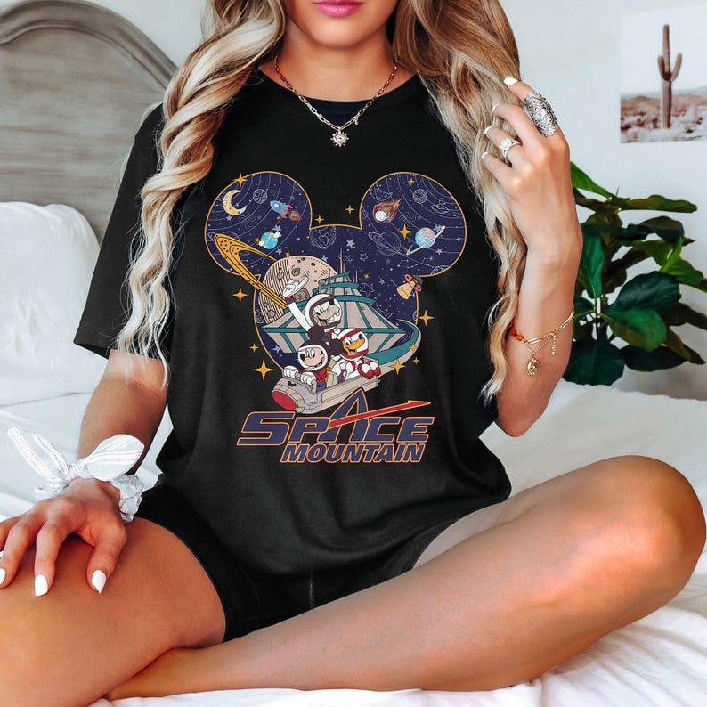 May include: Black t-shirt with a graphic of Mickey Mouse and friends riding a roller coaster in space. The graphic is inside a Mickey Mouse head silhouette. The text "Space Mountain" is below the graphic.