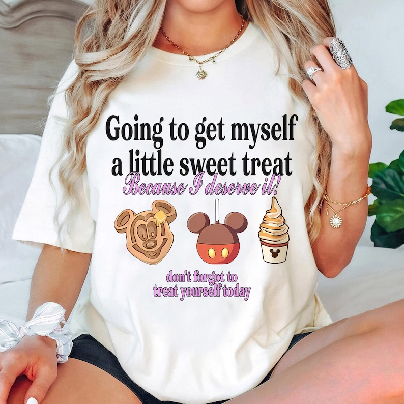 Puede incluir: Camiseta color crema con el texto "Going to get myself a little sweet treat Because I deserve it!" e ilustraciones de un gofre de Mickey Mouse, una manzana caramelizada y helado. Tambi&eacute;n est&aacute; presente la frase "don't forget to treat yourself today".