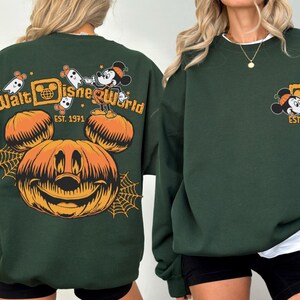 May include: Dark green sweatshirt featuring a Halloween-themed design. The front displays a Mickey Mouse graphic with "Est. 1971". The back has a large jack-o'-lantern, Mickey Mouse, ghosts, and the words "Walt Disney World".