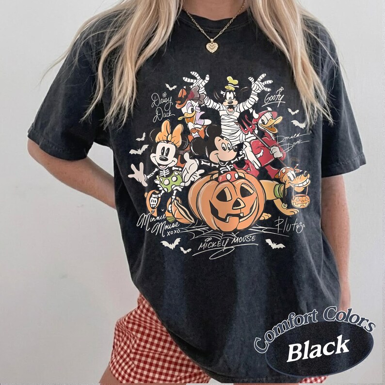 May include: A black acid-wash t-shirt featuring a Halloween-themed graphic of Disney characters including Mickey Mouse, Minnie Mouse, Donald Duck, Daisy Duck, Goofy, and Pluto. The characters are dressed in costumes around a large orange pumpkin.