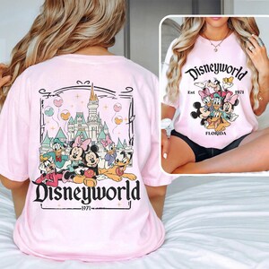 Puede incluir: Camiseta rosa con un gr&aacute;fico de Mickey Mouse y sus amigos frente al Castillo de Cenicienta. El texto "Disneyworld Est. 1971 Florida" est&aacute; impreso en la camiseta.