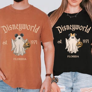 May include: Two t-shirts, one orange and one black, featuring a Disneyworld design. The design includes a ghost with Mickey Mouse ears holding a pumpkin, the text "Disneyworld est. 1971 FLORIDA".