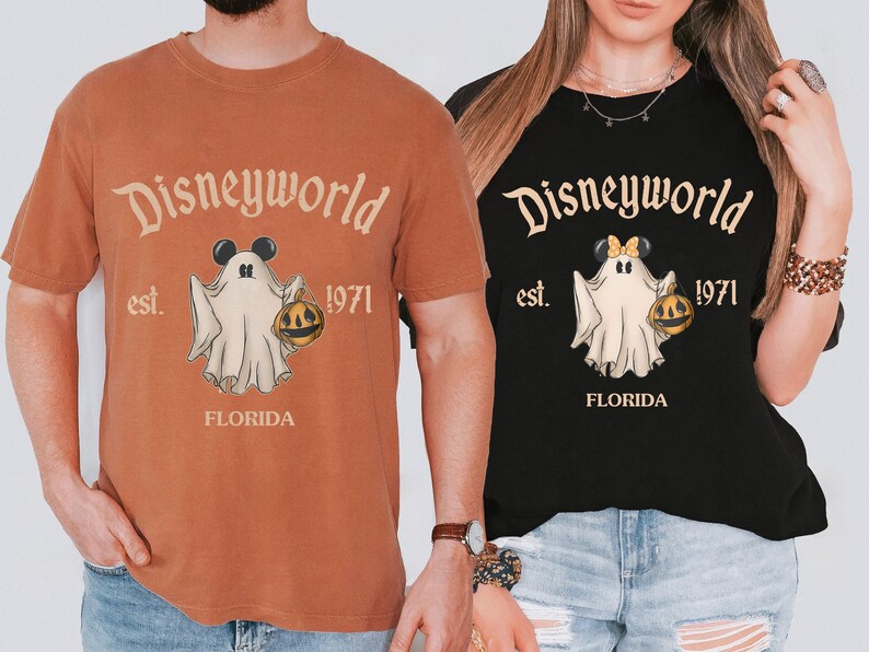 May include: Two t-shirts, one orange and one black, featuring a Disneyworld design. The design includes a ghost with Mickey Mouse ears holding a pumpkin, the text "Disneyworld est. 1971 FLORIDA".