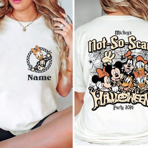 May include: Cream-colored t-shirt featuring Daisy Duck in a circular design with the word "Name" below. The back of the shirt displays Mickey Mouse and friends with the text "Mickey's Not-So-Scary Halloween Party 2026".