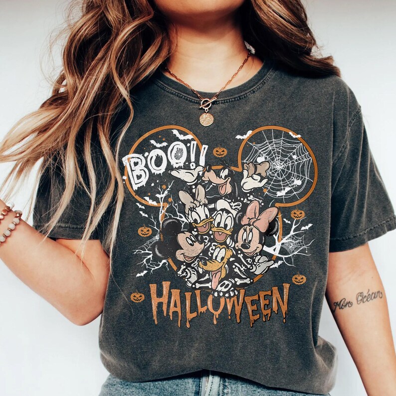 K&ouml;nnte beinhalten: Dunkelgraues T-Shirt mit einem Halloween-Design mit Micky Maus, Donald Duck, Daisy Duck, Minnie Maus und Goofy. Das Shirt hat das Wort "BOO!!" &uuml;ber den Figuren und "HALLOWEEN" darunter, mit Spinnweben und K&uuml;rbissen.