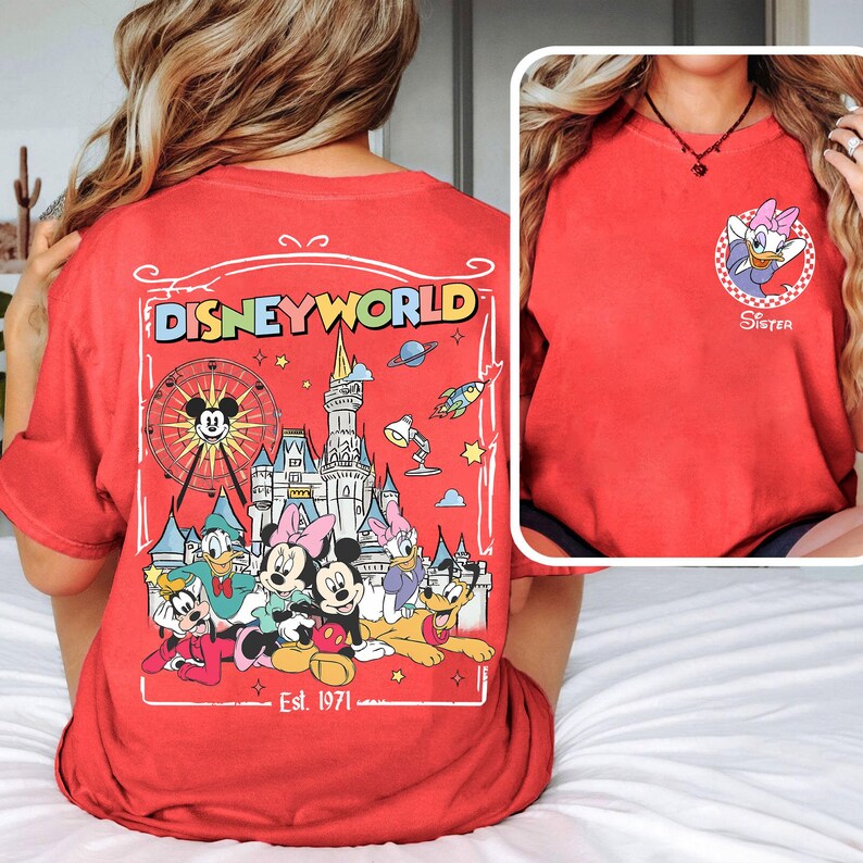 Op de afbeelding: Rood T-shirt met een Disney World-afbeelding op de rug, met Mickey Mouse, Minnie Mouse, Donald Duck en andere personages. De voorkant van het shirt heeft een Daisy Duck-afbeelding met het woord "Sister". Het shirt heeft een comfortabele pasvorm.
