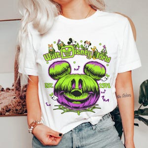 May include: White t-shirt featuring a Halloween-themed Walt Disney World design. The graphic includes a green and purple Mickey Mouse pumpkin, the text "Walt Disney World", and the year "1971". Additional characters and spooky elements are also present.